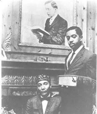 A young Warith Deen Mohammed holding the holy book beneath a portrait of W. D. Fard, the Nation's founder. Photographer unknown.