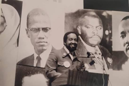 Warith Deen Mohammed speaks beneath portraits of Malcolm X, Marcus Garvey and Martin Luther King Jr. Photographer unknown.